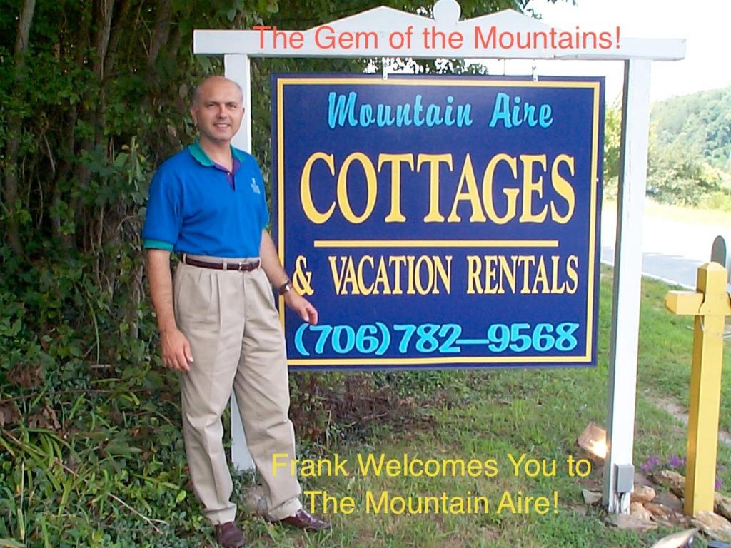 Un uomo è in piedi davanti a un cartello di Mountain Aire Cottages & Inn a Clayton