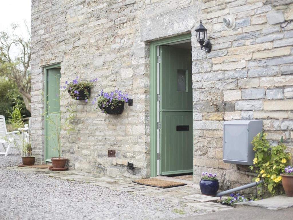 a stone building with a green door and flowers at Withy Cottages in Langport