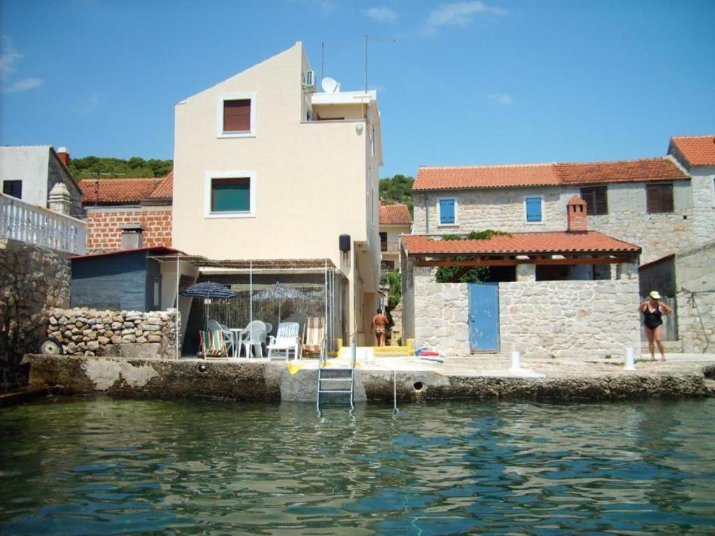 a house sitting on the water next to a building at Apartment Mirni - 5 m from sea in Prvić Luka