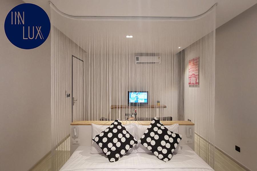 1 dormitorio con 1 cama con almohadas blancas y negras en INNLUXPHUKET, en Ban Laem Hin