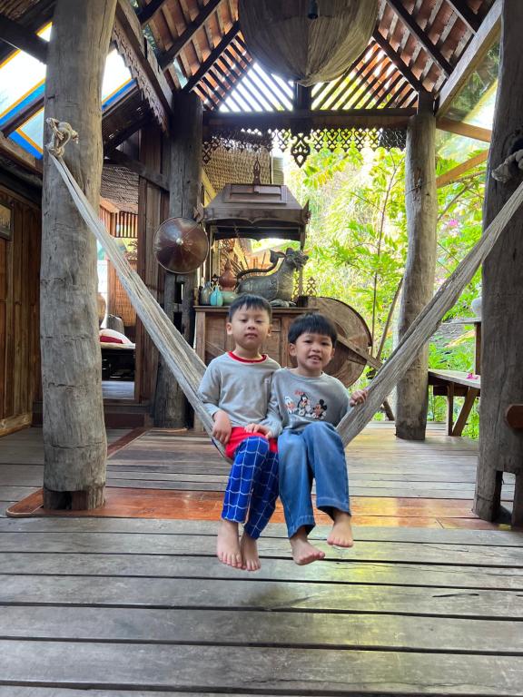 dos chicos sentados en un columpio en un porche en Baan Boo Loo Village- SHA Plus en Chiang Mai