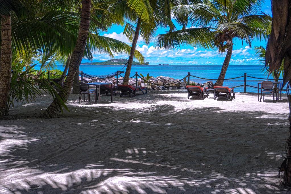 a beach with chairs and palm trees and the ocean at Anse Kerlan Beach Chalets in Anse Kerlan