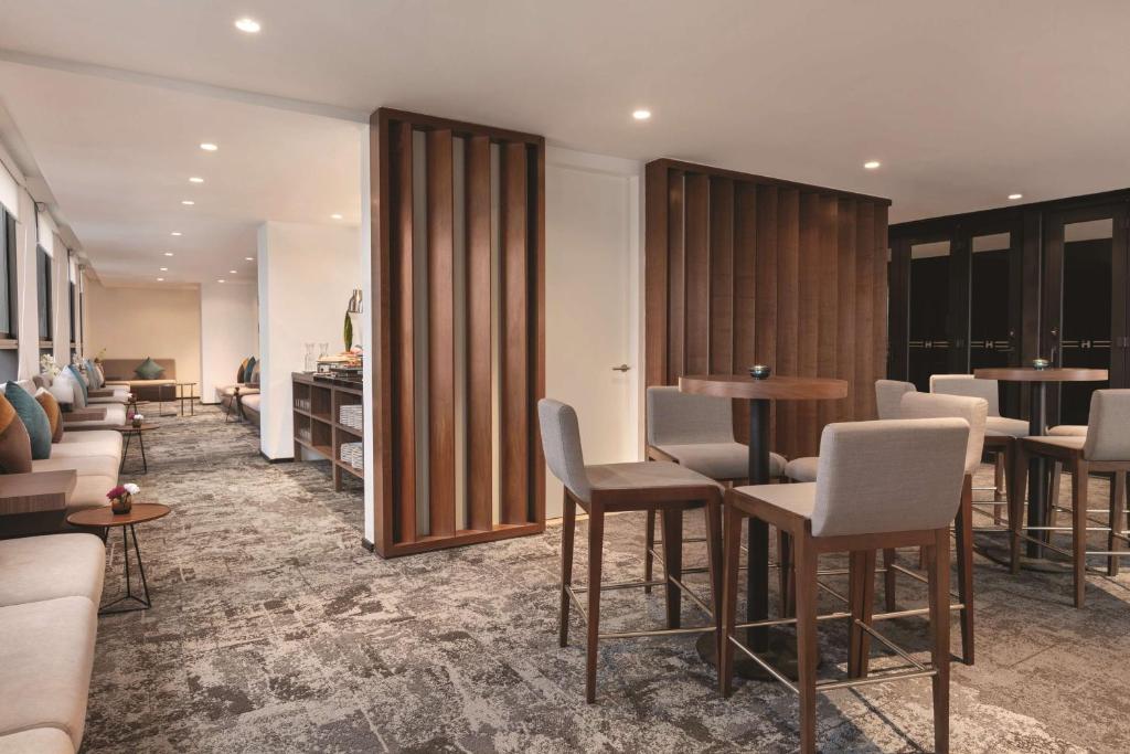 A bright hotel lounge with small tables, upholstered chairs, and a carpeted seating area.