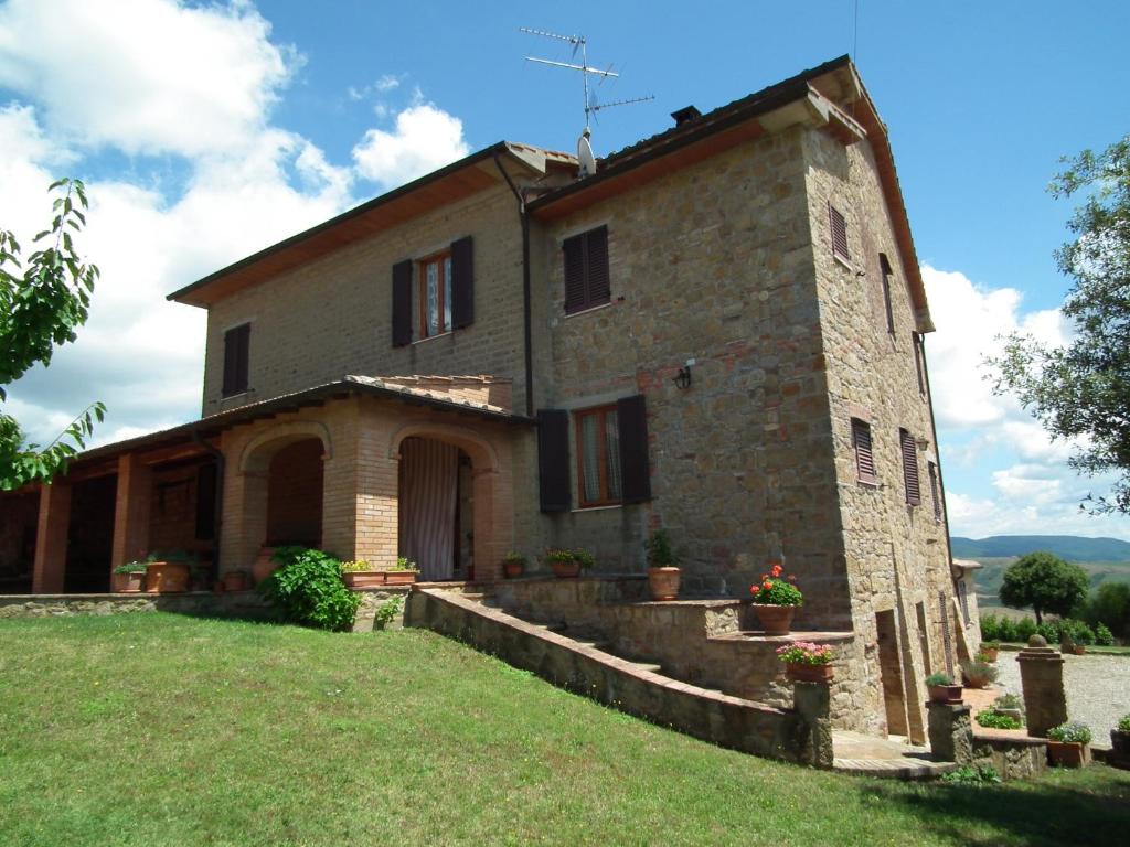 um antigo edifício de pedra com um campo relvado à frente em Agriturismo Riposati em Monticchiello