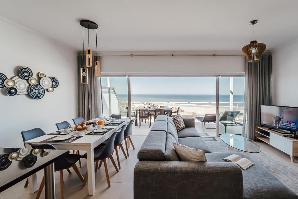 un salon avec un canapé et une salle à manger avec la plage dans l'établissement Beachfront Atlantic Sunset A07, à Óbidos