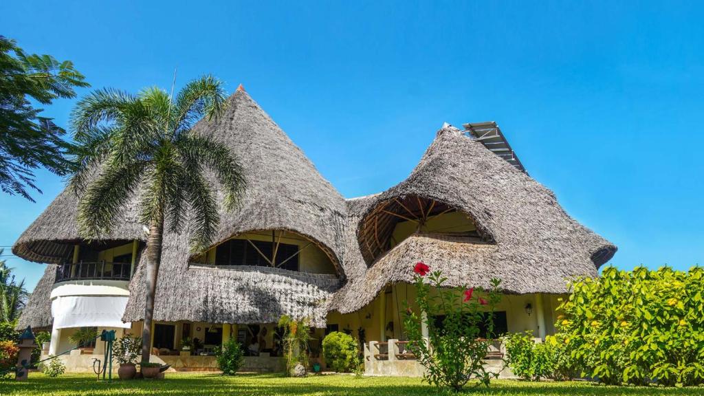 una casa con techo de paja y una palmera en Amani Paradise - Luxury Villas, en Diani Beach