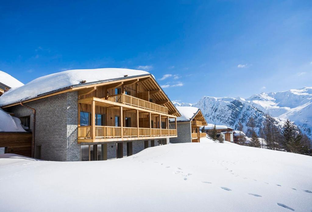 un grand bâtiment dans la neige avec des montagnes dans l'établissement TERRESENS - Le Hameau de Barthélémy, à La Rosière