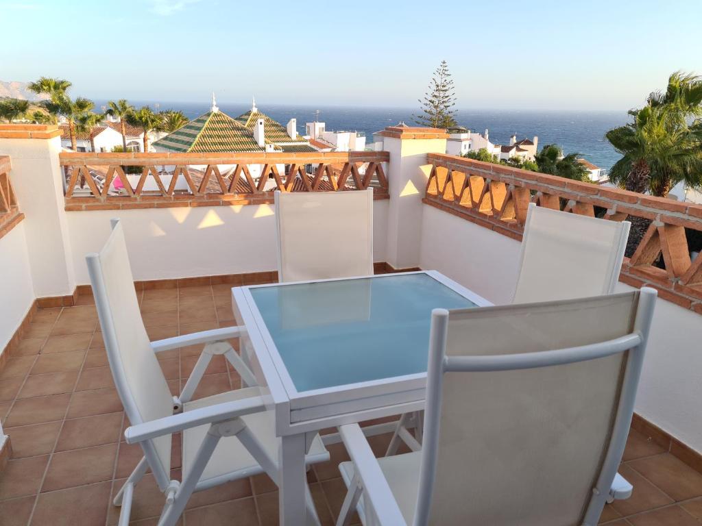 una mesa de cristal y sillas en un balcón con vistas al océano en APARTAMENTO BONITO EN PINAL DEL MAR NERJA, en Nerja