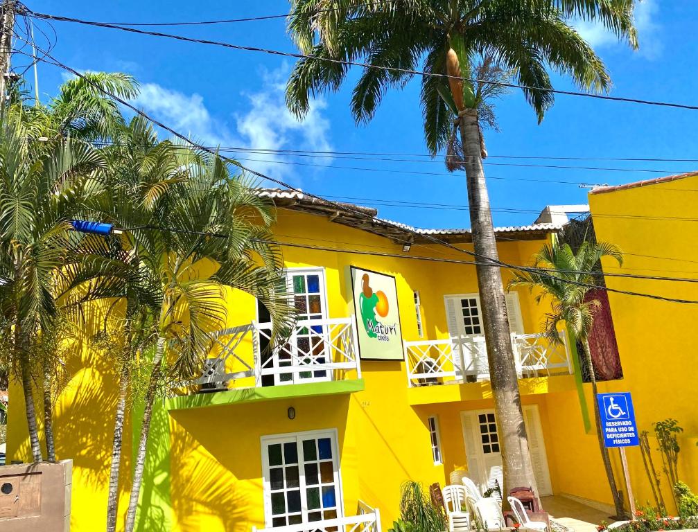 a yellow building with palm trees in front of it at MATURI CENTRO in Pipa