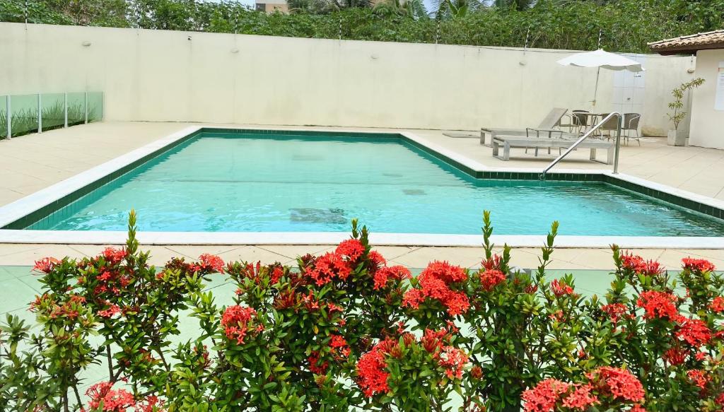 a swimming pool with a chair and red flowers at Cobertura Duplex: piscina, três quartos e beira á mar in Ilhéus