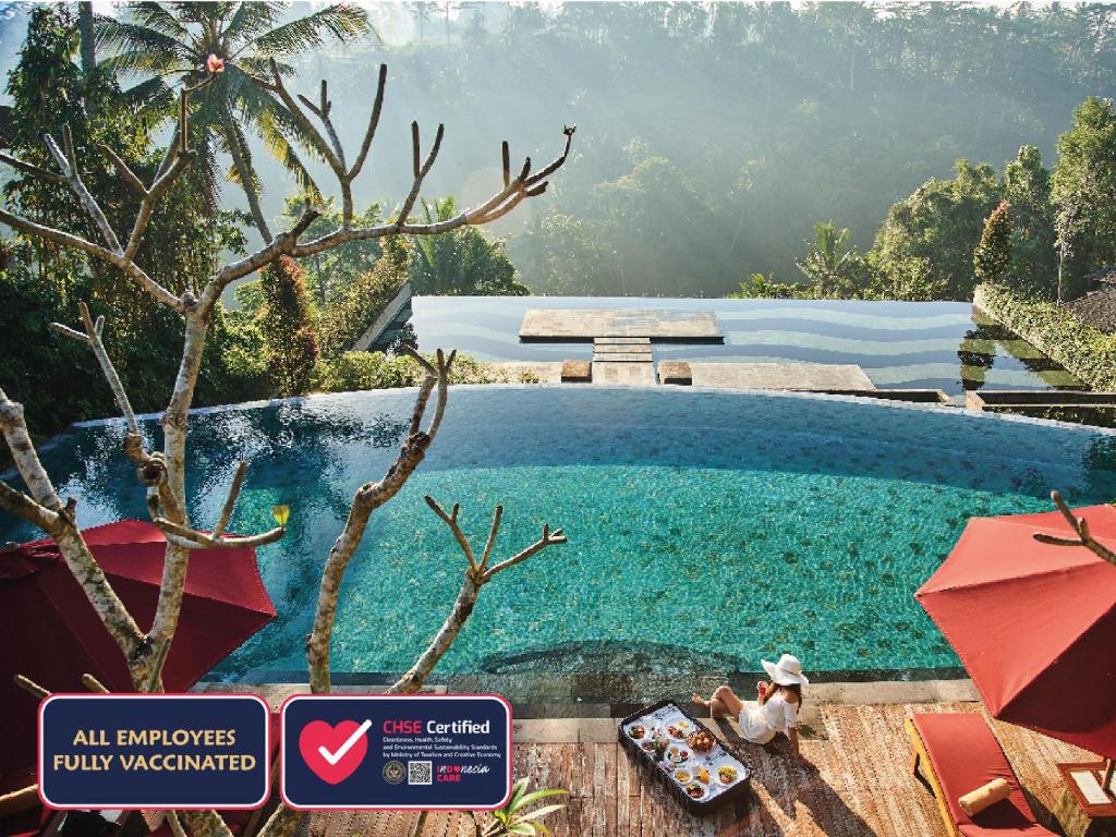 a pool at a resort with a woman sitting on a chair at Jannata Resort and Spa in Ubud