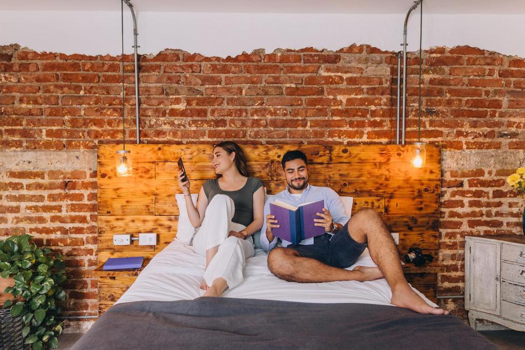 a man and woman sitting on a bed reading a book at Septimo Hostal in Querétaro