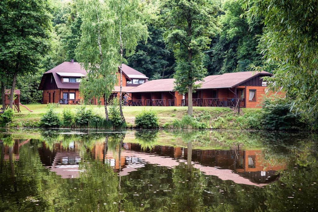 Drewniane domki nad stawem odbijające się w wodzie, w otoczeniu drzew