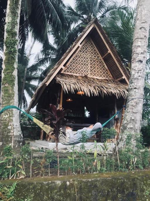 une petite cabane avec une personne assise sur un hamac à l'avant dans l'établissement Saung Batukaras, à Tjidjulang