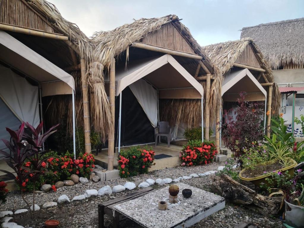 un complejo con un edificio con techo de paja con una mesa y flores en El Nómada Hostel, en Palomino