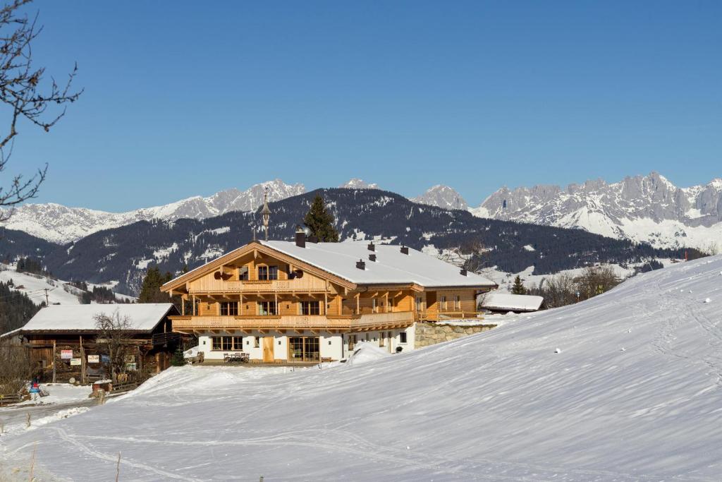 a large wooden house on top of a snow covered slope at Schrolln Appartements in Kirchberg in Tirol