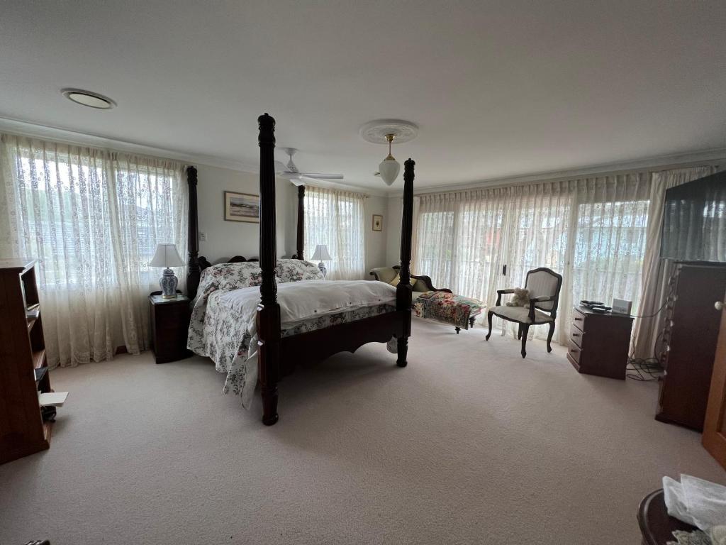 a bedroom with a bed and a chair and windows at Luxury 4 bedroom house in Deewhy