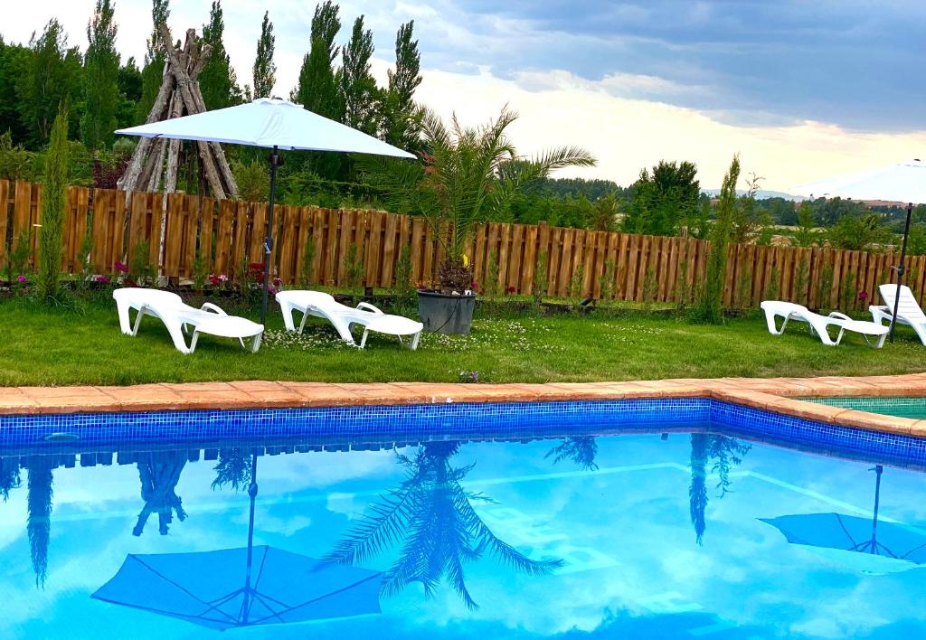 a group of white chairs and an umbrella next to a pool at El BURGO DE OSMA ALOJAMIENTO RURAL VILLA BAGH in El Burgo de Osma