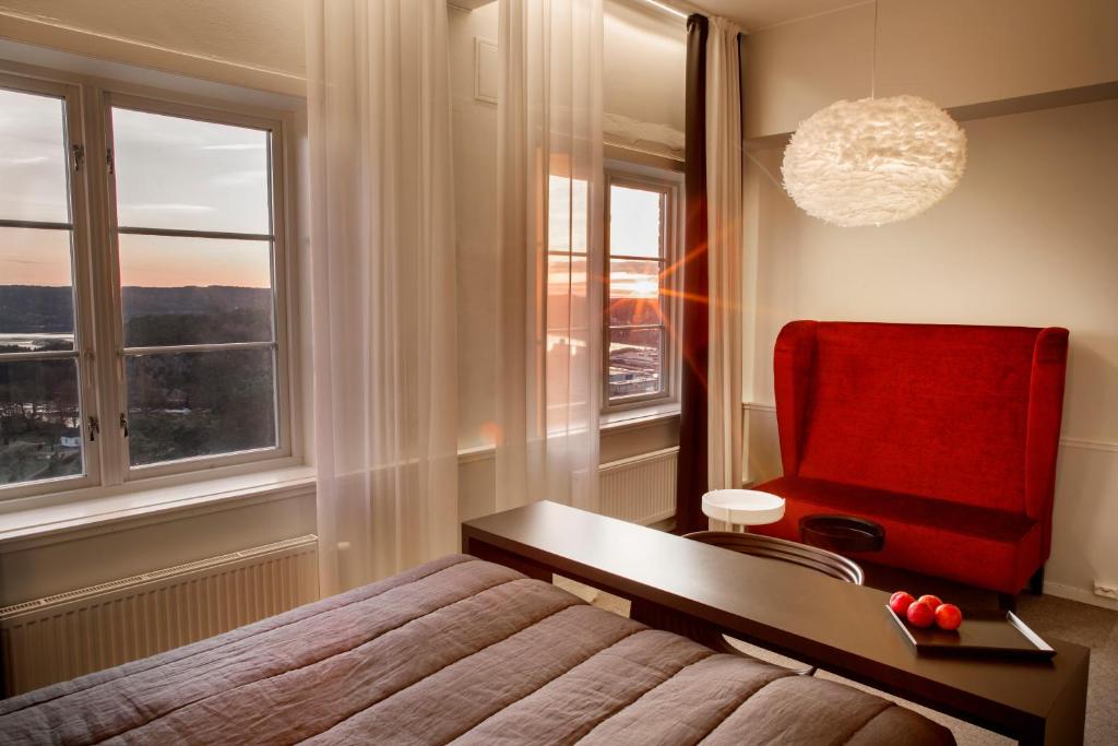 a bedroom with a bed and a red chair and window at Fredriksten Hotell in Halden