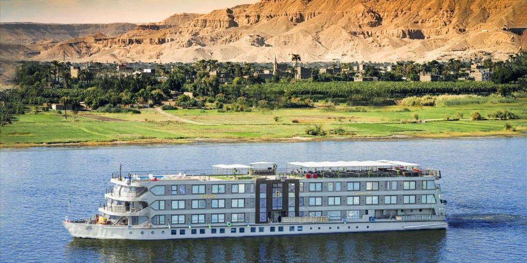 a cruise ship on the water next to a building at Historia The Boutique Hotel Nile Cruise - Every Monday from Luxor for 04 & 07 Nights - Every Friday From Aswan for 03 & 07 Nights in Luxor