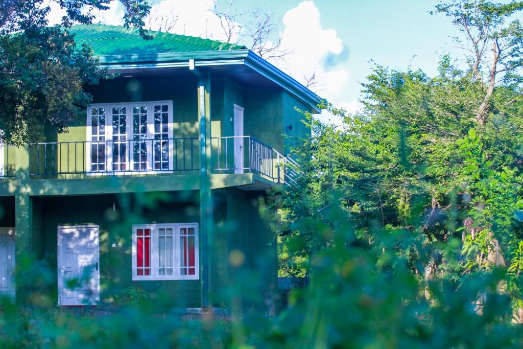 a green house with a balcony and a red door at Pavona Lake in Sigiriya