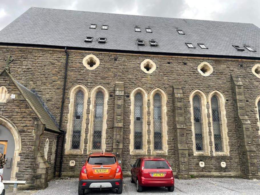 Dowlais的住宿－Old St Johns Church，两辆汽车停在一座大型砖楼前