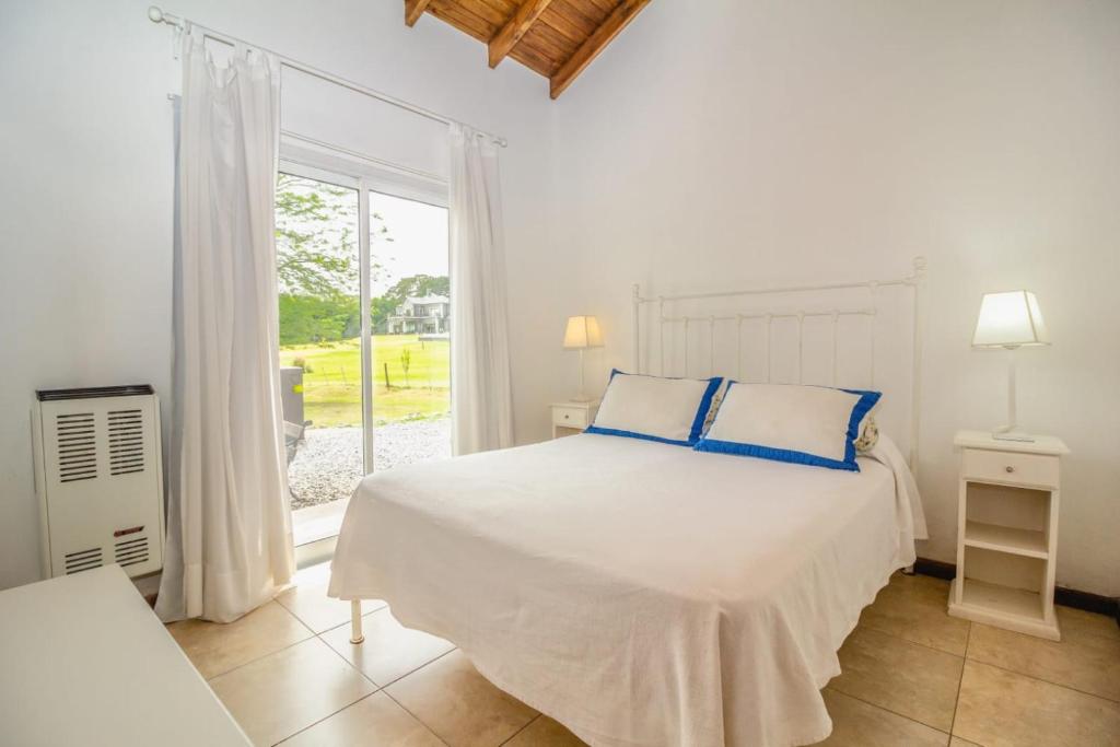 a white bedroom with a bed and a window at Abril Village in Tandil