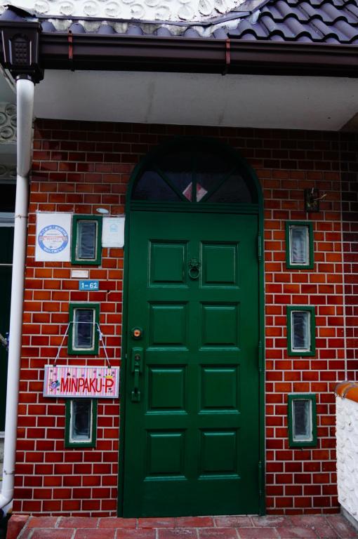 una puerta verde en un edificio de ladrillo con un cartel en MINPAKU-P 民泊p, en Izumisano