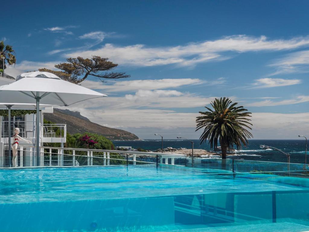 a swimming pool with an umbrella and the ocean at South Beach Camps Bay Boutique Hotel in Cape Town