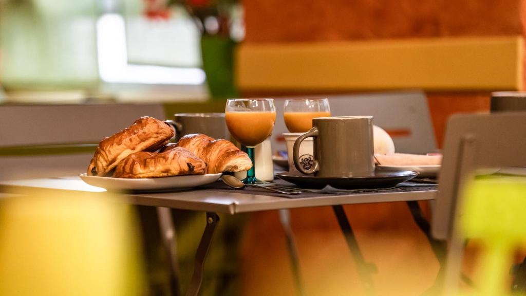 una mesa con un plato de pan y vasos de zumo de naranja en Hôtel Furania en Saint-Étienne