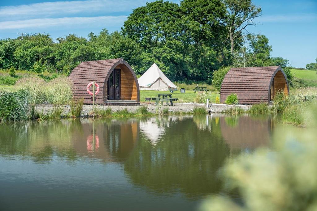 duas cabanas de madeira junto a um lago com uma tenda em Parc Maerdy Glamping Holidays em New Quay