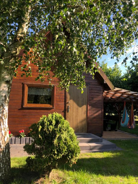 a wooden house with a door and a tree at DREWNIANE DOMKI pod brzozami in Karwia