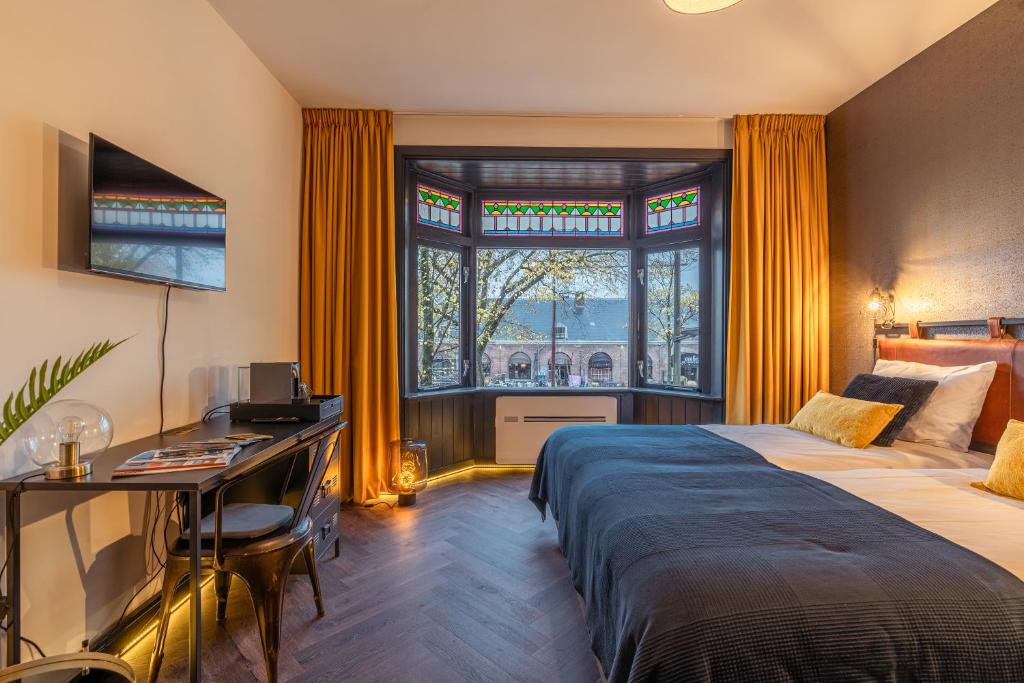 a bedroom with two beds and a desk and a window at Hotel De Werf in Den Helder