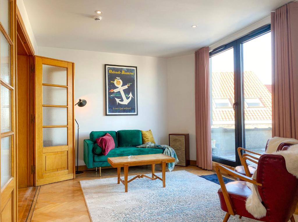 Una sala de estar con un sofá verde y una mesa. en Family Floor - La Couronne Oostende - Authentiek appartement met veel lichtinval, en Ostende