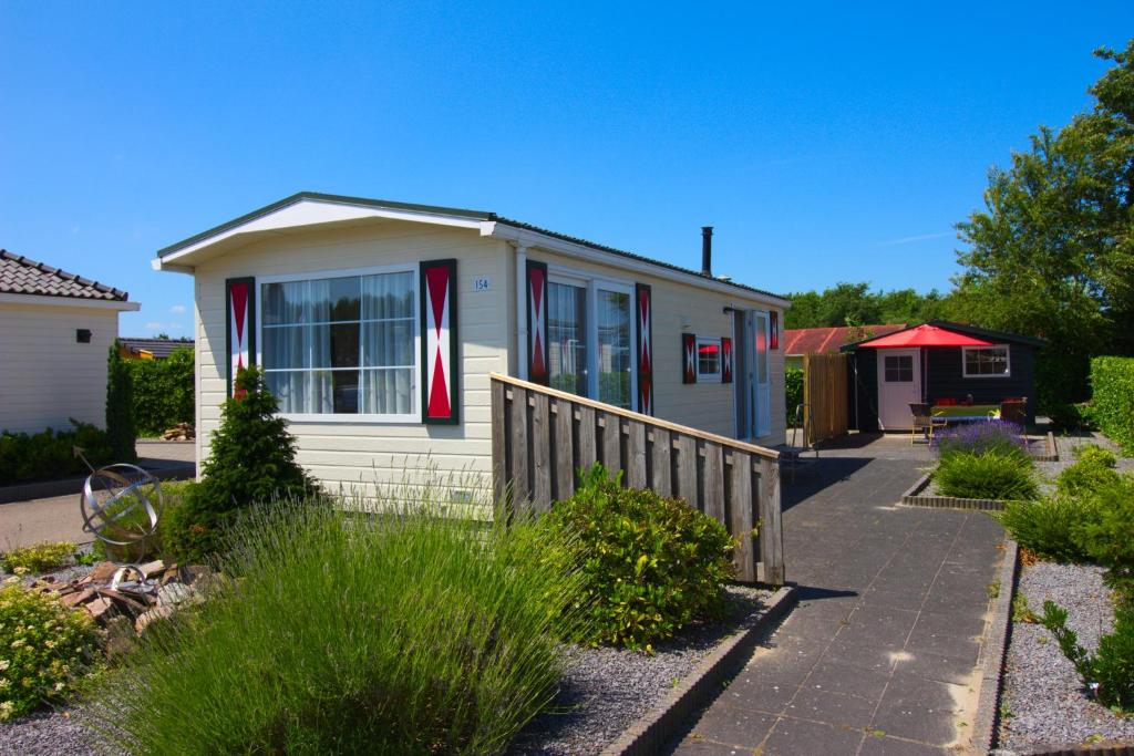 a small white house with red doors and a fence at Chaletparc Krabbenkreek Zeeland - Chalet 154 in Sint Annaland