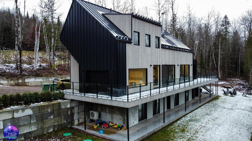 une maison avec un toit noir et un balcon dans l'établissement Chalet Flodhaus- Bord Rivière St-Maurice (navigable) / SPA /SAUNA - Chalets Galaxia, à Saint Roch de Mekinac