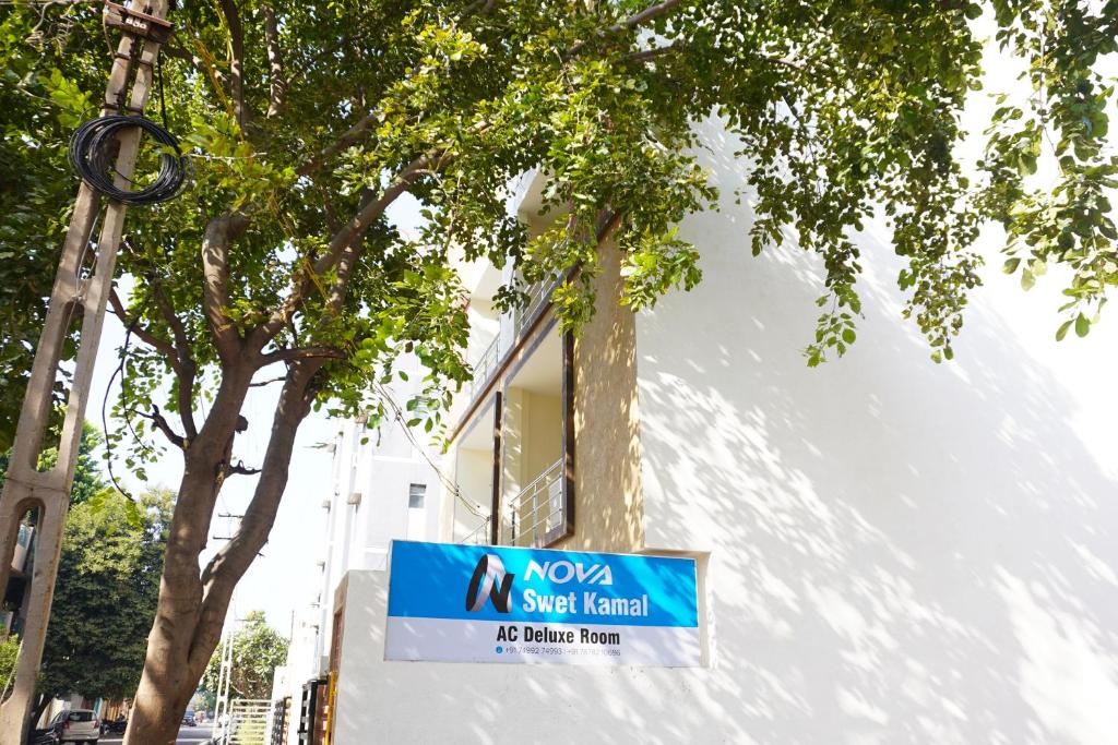 a sign in front of a building with a tree at Hotel Nova SK in Rajkot