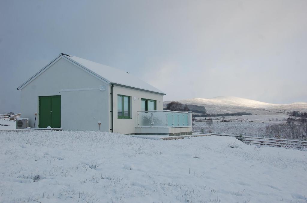 una casa blanca con una puerta verde en la nieve en Glas Beag en Spean Bridge