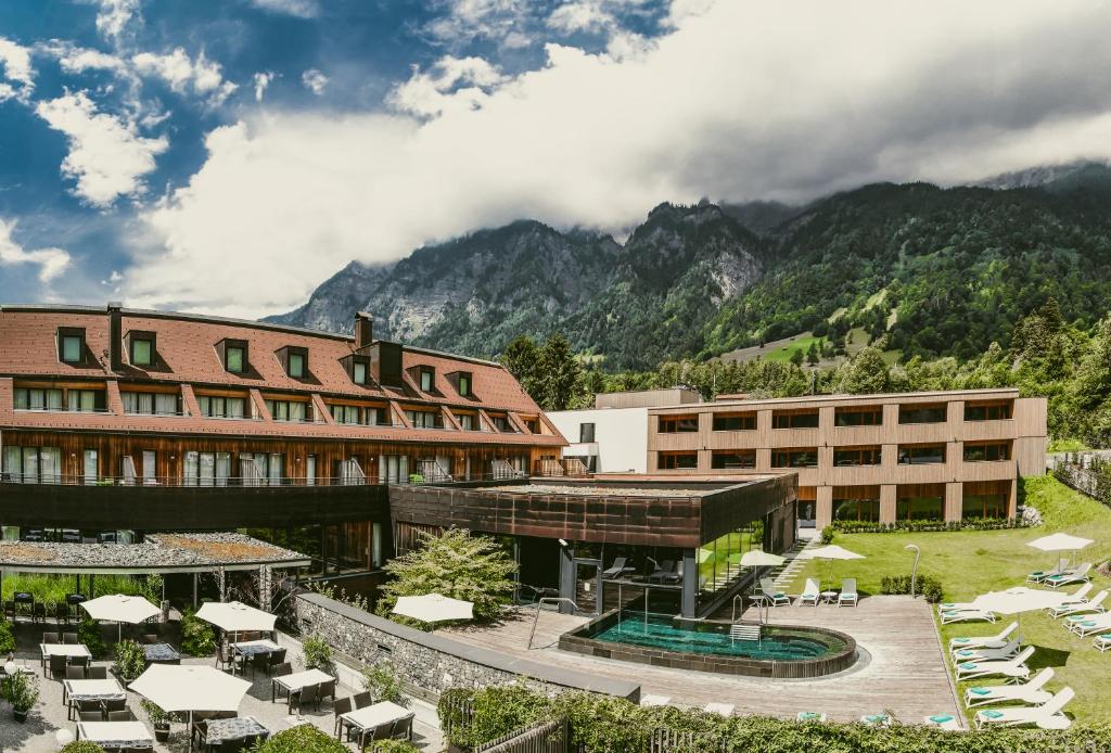 ein Hotel mit Tischen und Stühlen vor einem Berg in der Unterkunft TRAUBE BRAZ Alpen Spa Golf Hotel in Bludenz