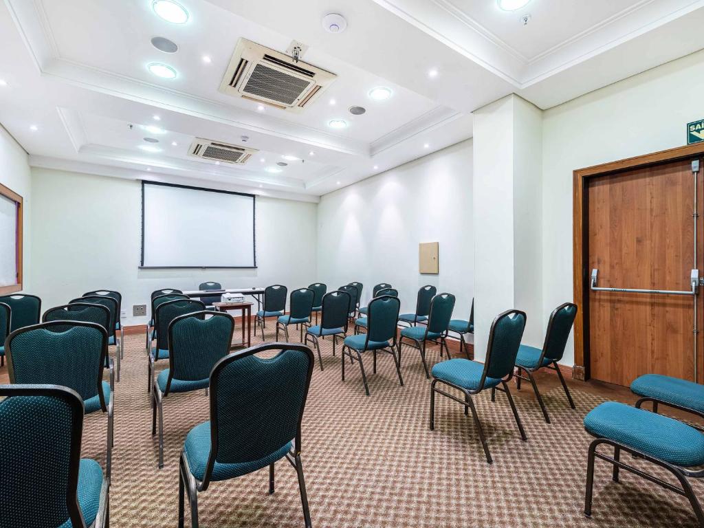 a conference room with chairs and a podium and a screen at Hotel Cassino Tower Campinas Cambuí By Nacional Inn in Campinas
