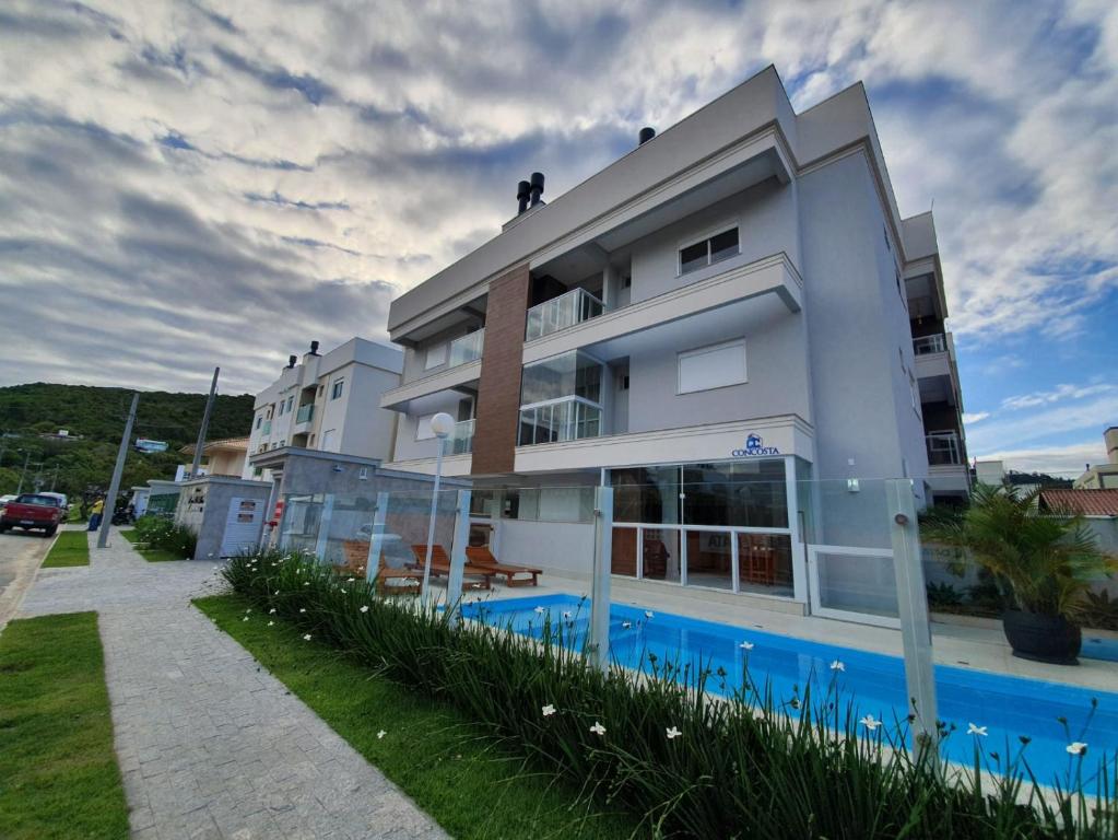 um edifício branco com uma piscina em frente em Apto na praia de Palmas, próximo ao mar, climatizado e com piscina em Governador Celso Ramos