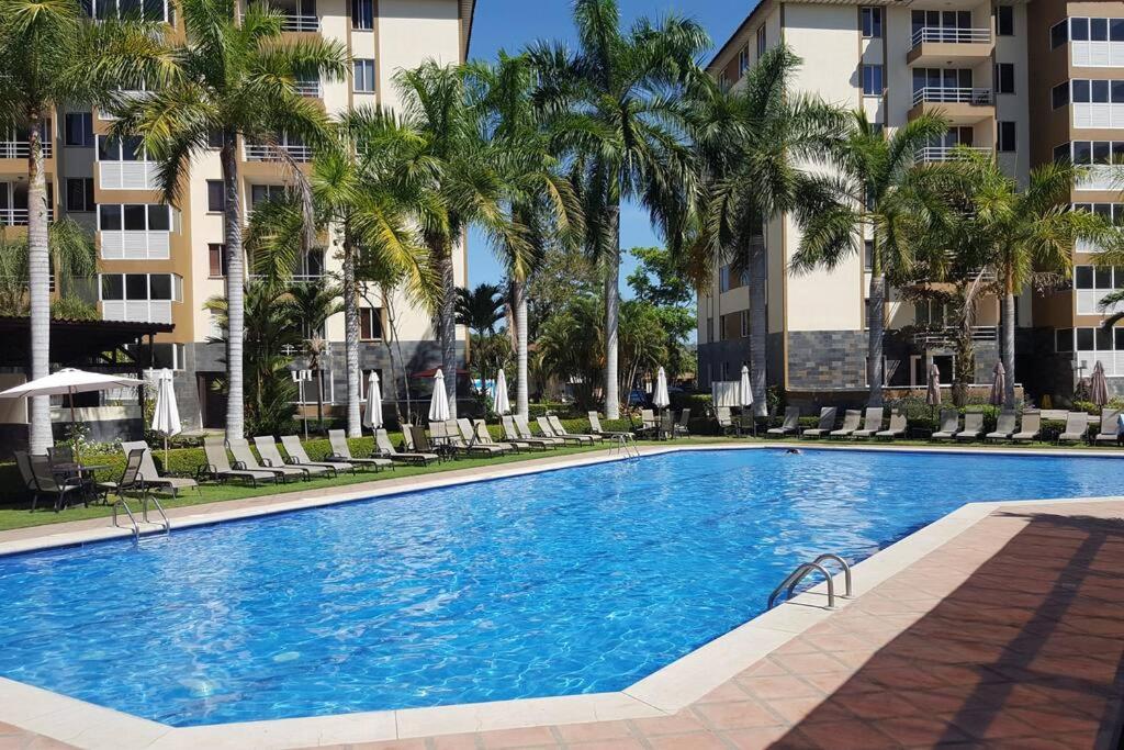 - une piscine avec des chaises, des palmiers et des bâtiments dans l'établissement Oceanview 6th Floor Jaco Condo, à Jacó