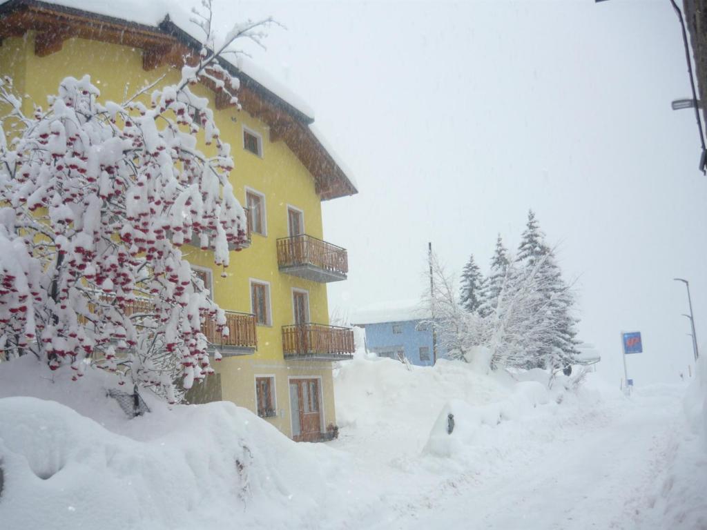 żółty budynek pokryty śniegiem obok drzewa w obiekcie Appartamenti Mosconi Mistica w mieście Vermiglio