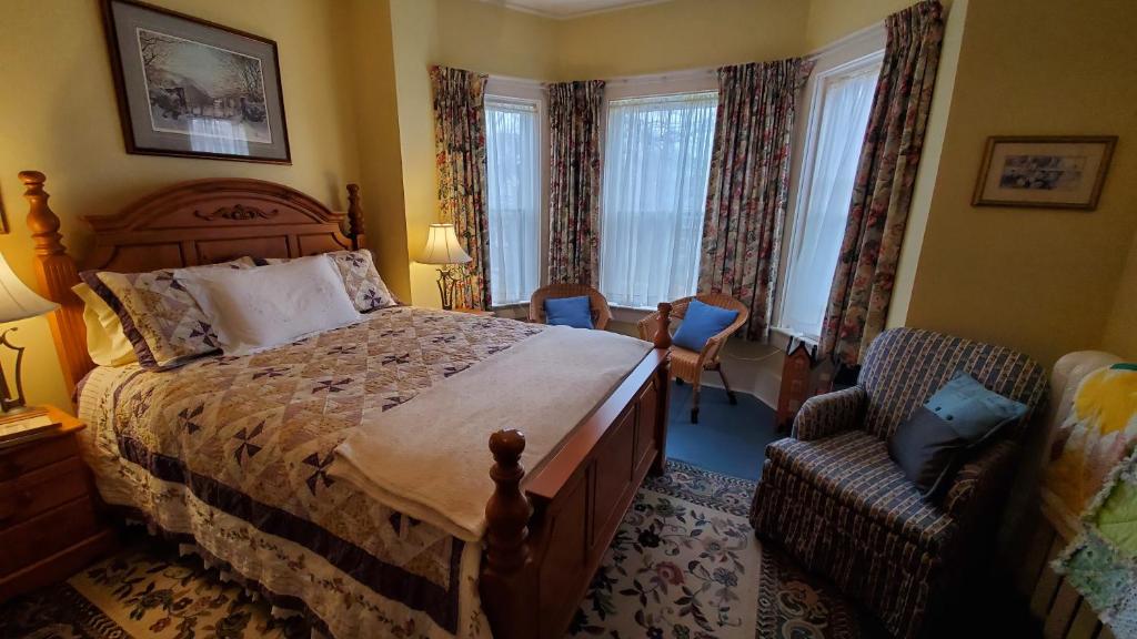 a bedroom with a bed and a chair and windows at The Lark & Loon Inn in Annapolis Royal