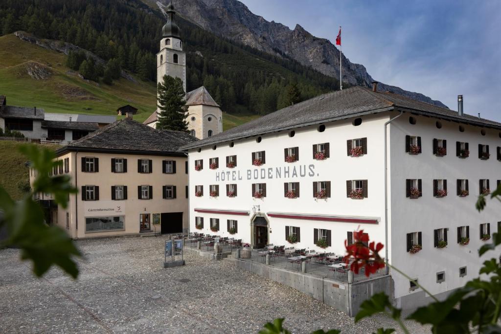 a large white building with a church and a mountain at Hôtel Bodenhaus in Splügen