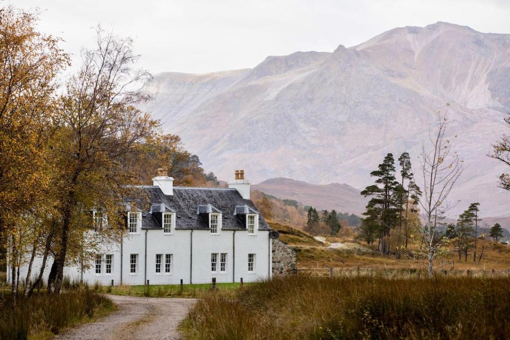 a white house on a dirt road with mountains in the background at Coulin Farmhouse in Kinlochewe