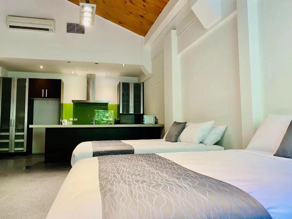 two beds in a hotel room with a kitchen at Gamma Hotel in Auckland