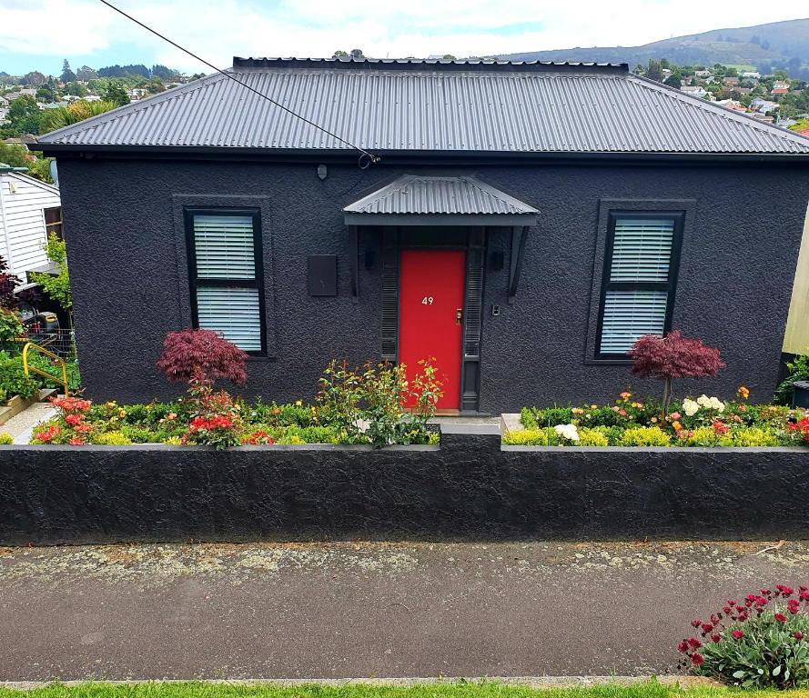 ein schwarzes Haus mit einer roten Tür und ein paar Blumen in der Unterkunft Roslyn Business Studio - 2 bedroom in Dunedin