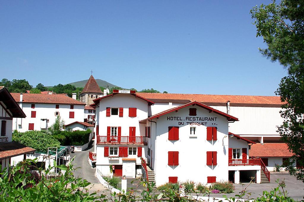 a white building with red shuttered windows in a town at Hôtel Le Trinquet in Louhossoa