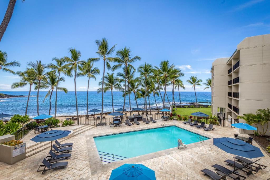 a swimming pool with palm trees and the ocean at Aston Kona By The Sea in Kailua-Kona